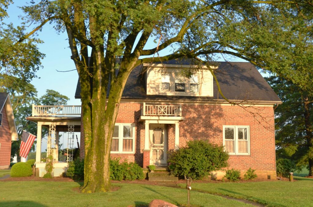 A red brick home under a large shade tree