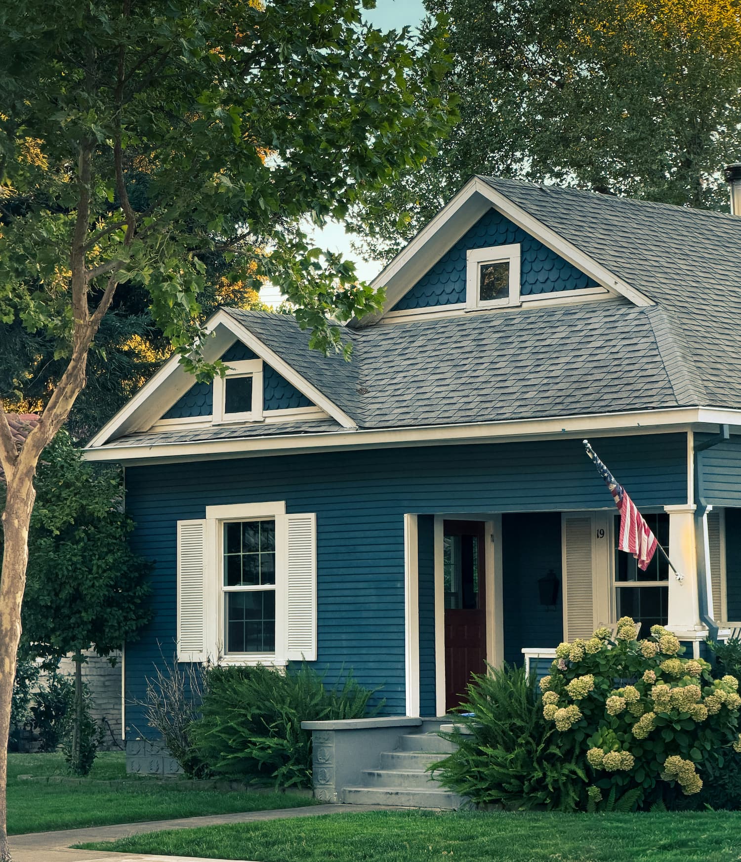 Blue cottage with white trim and a flag by the front door