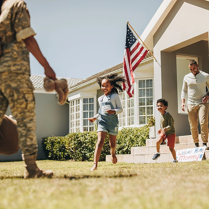 A service member arriving home to her children and husband outside their house, representing the military relocation help that runs alongside Jennifer Andrews' first time home buyer Indiana guide.