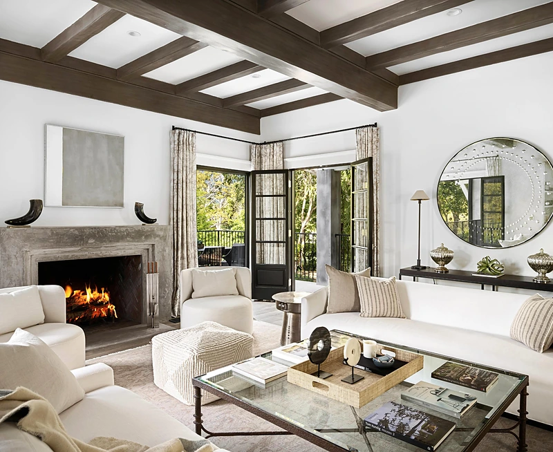 A living room with a lit fireplace, beamed ceiling and open French doors, representing the kind of interior buyers tour among Shelbyville Indiana homes for sale.